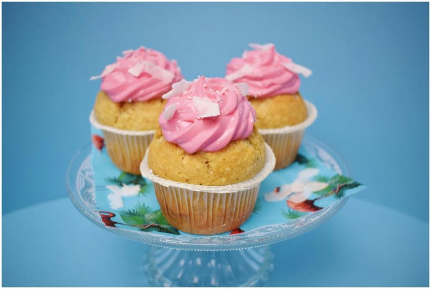 Three homemade cupcakes with pink frosting on a gl