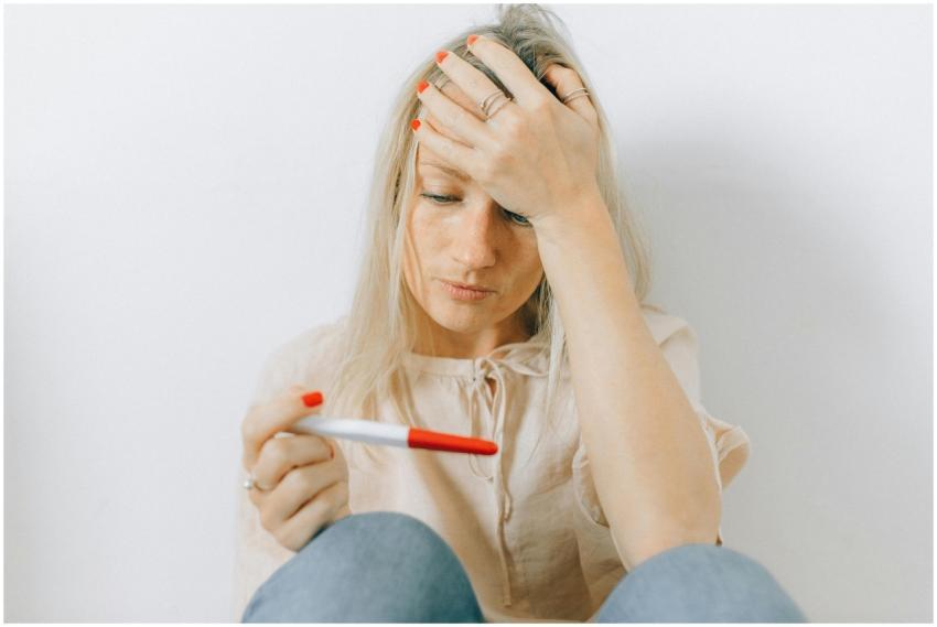 A concerned woman looks at a pregnancy test, refle