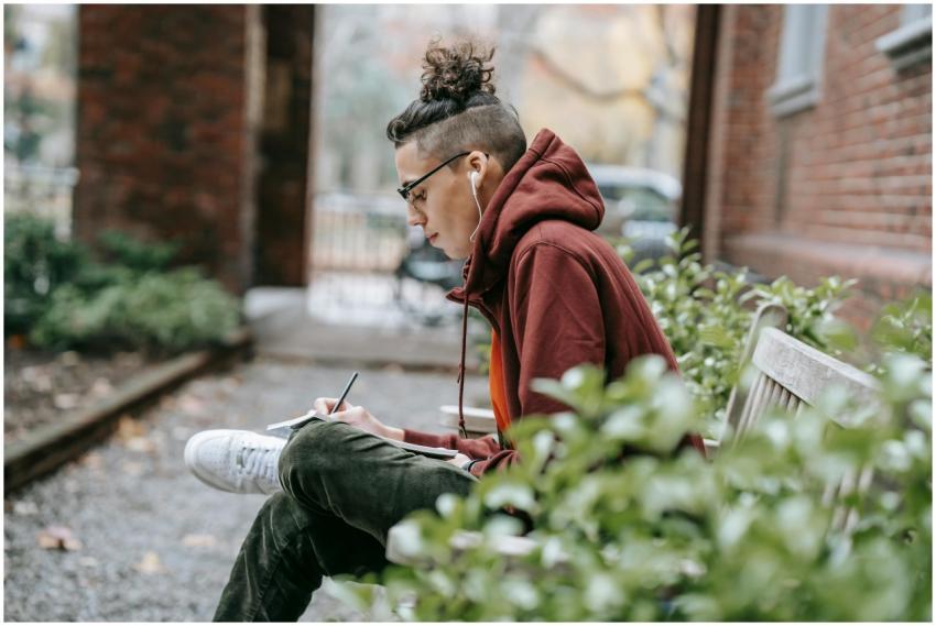 Pensive young man writing in a notebook while seat