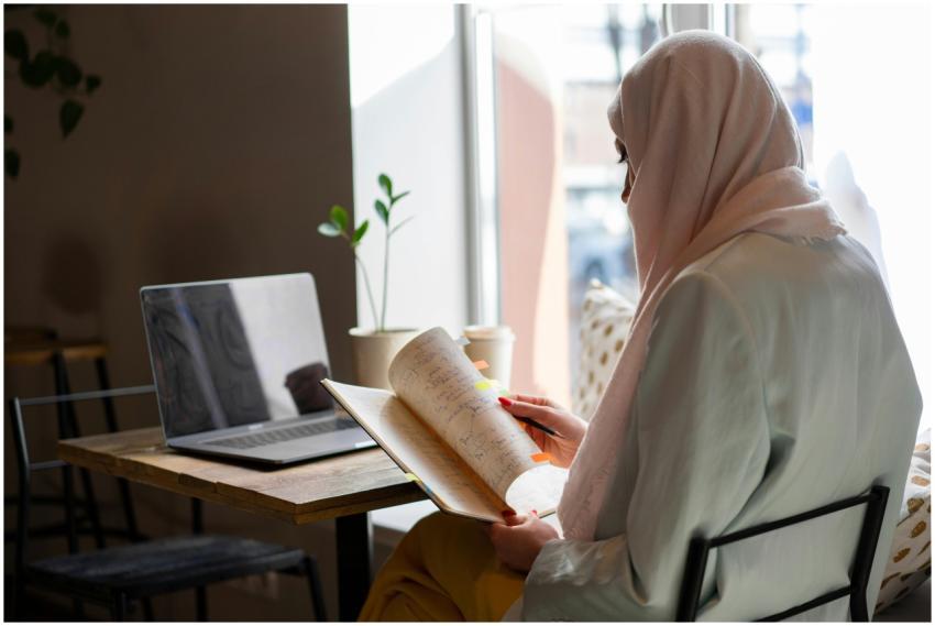 A woman in a hijab sits indoors by a window, readi