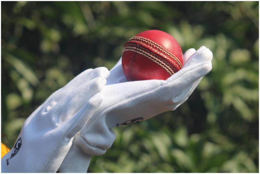 Detailed photo of a red cricket ball held by glove