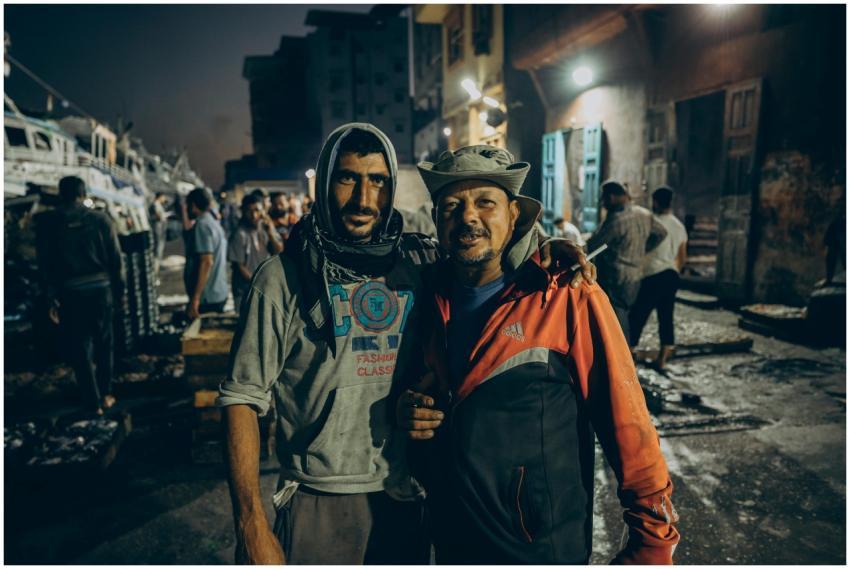 Two fishermen posing at a vibrant night fish marke
