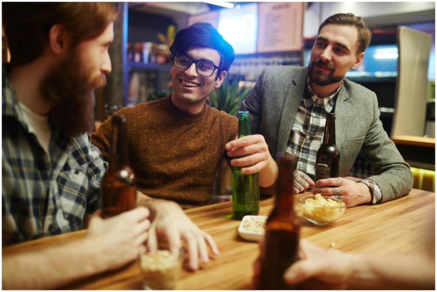 Three men smiling and enjoying beer together indoo