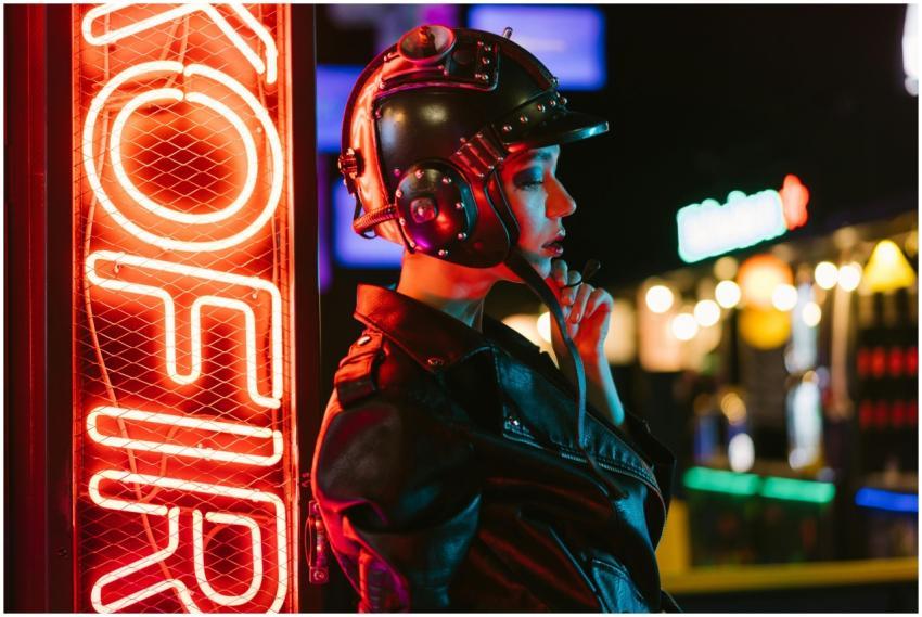 A stylish woman in a helmet poses by a neon sign,