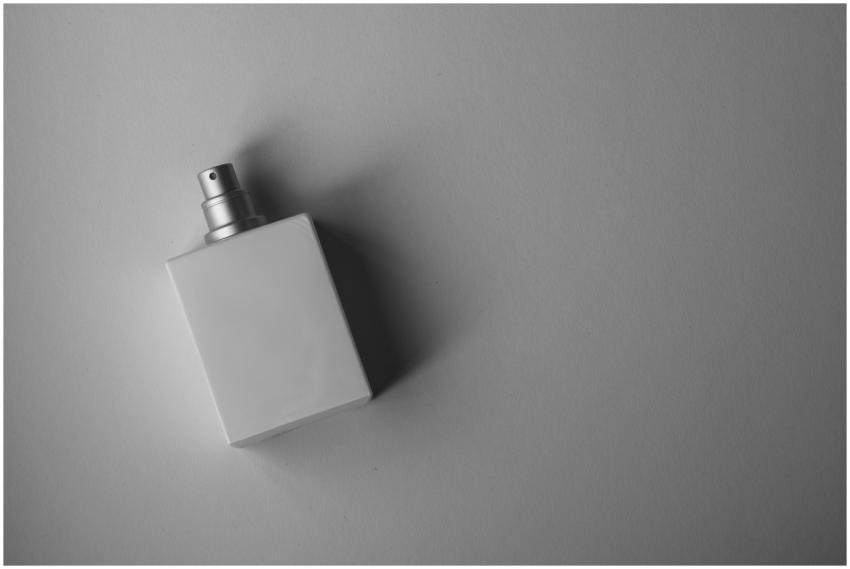 A sleek white perfume bottle photographed on a gra