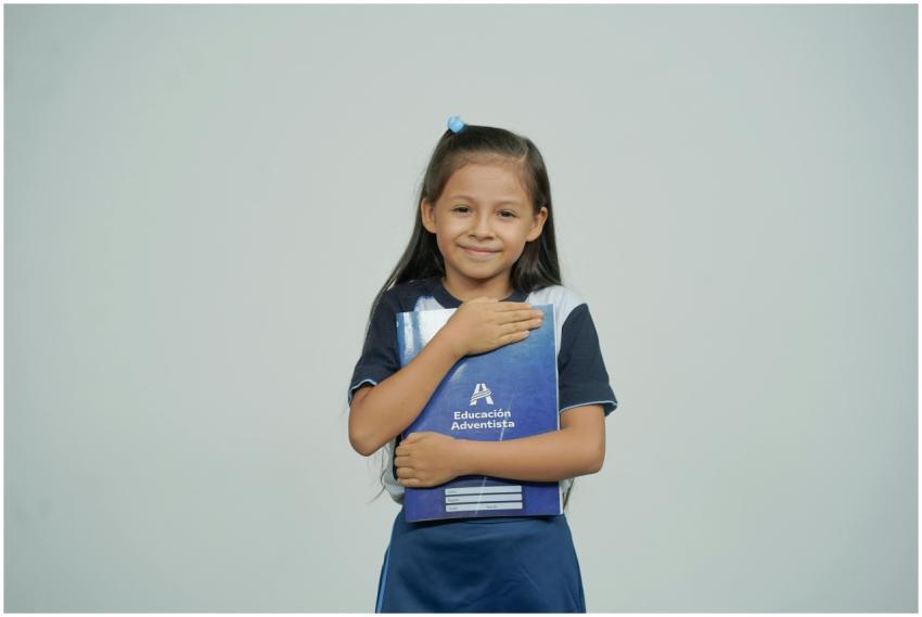 A young girl smiles while holding her school noteb