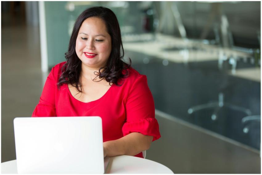 Asian woman smiling while working on a laptop in a