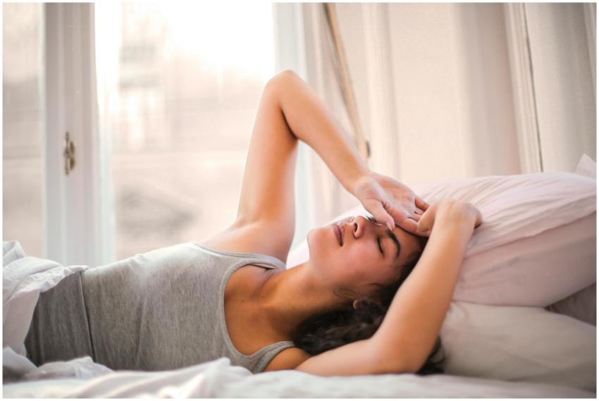 Woman in gray tank top resting on bed with natural