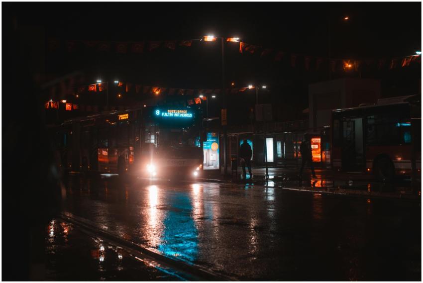A city bus illuminated in the night at a busy stat