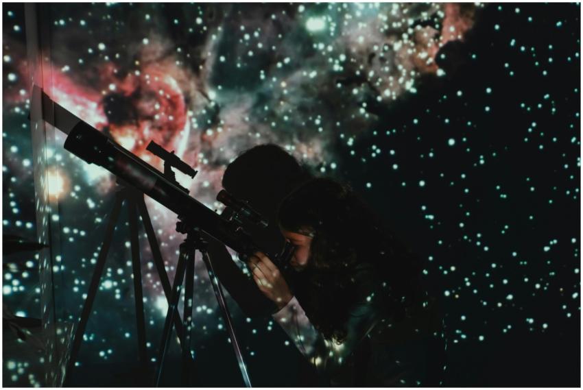 A girl looks through a telescope at a starry proje