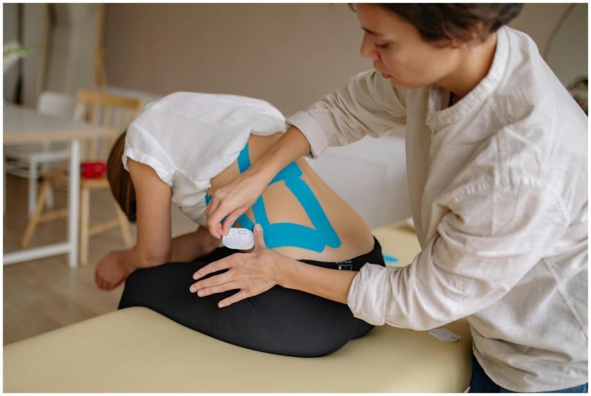 A therapist applies blue kinesiology tape to a pat