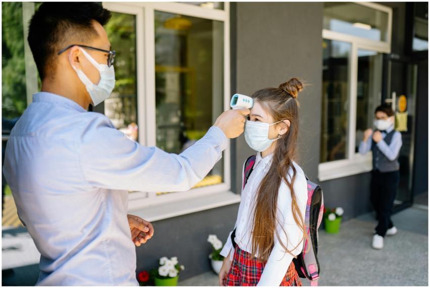 Masked teacher checks student's temperature with a