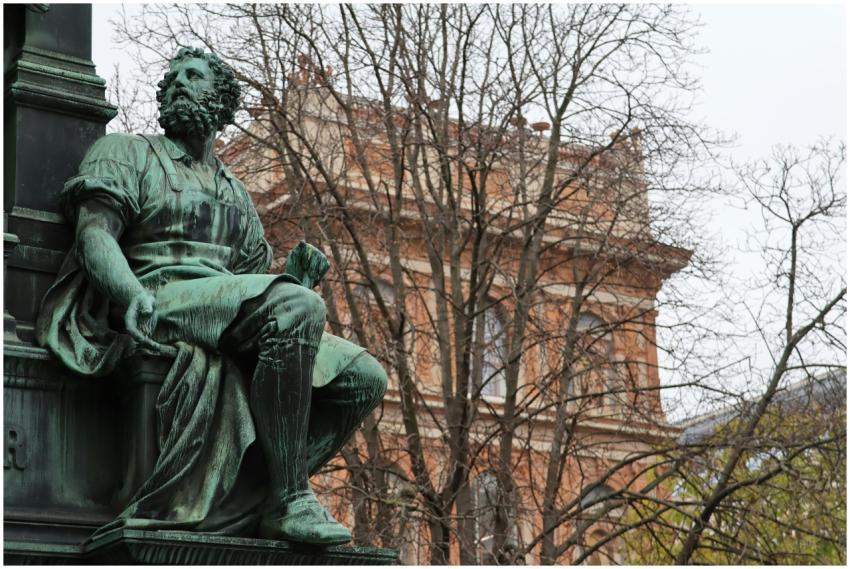 A bronze statue in Vienna with historic architectu