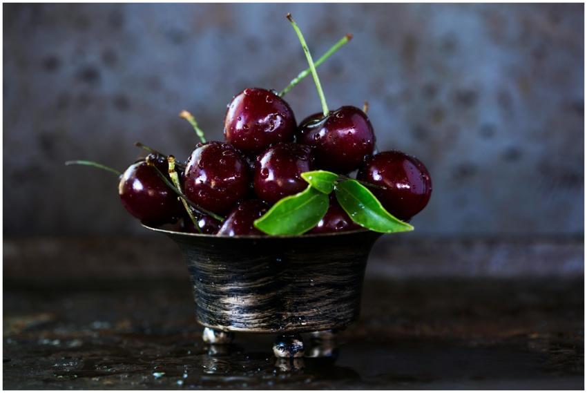 A rustic metal bowl filled with fresh, juicy cherr