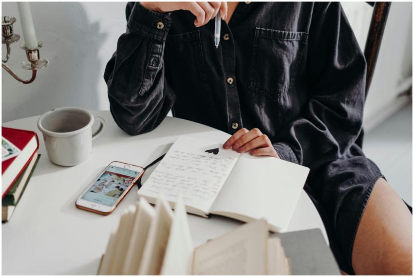 Woman seated indoors writing in a journal with cof