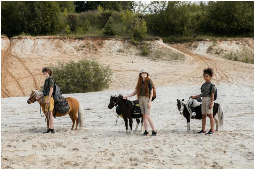 A group of children with ponies on a sandy outdoor