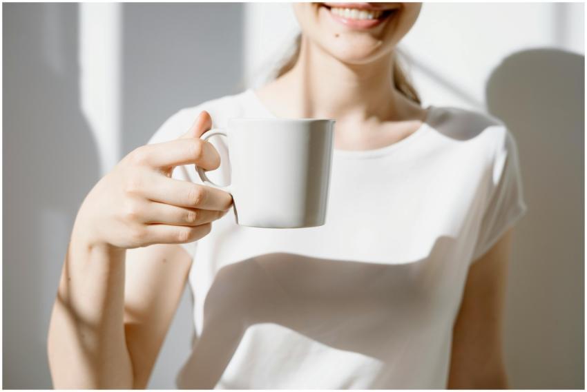 A smiling woman holds a white coffee cup in natura
