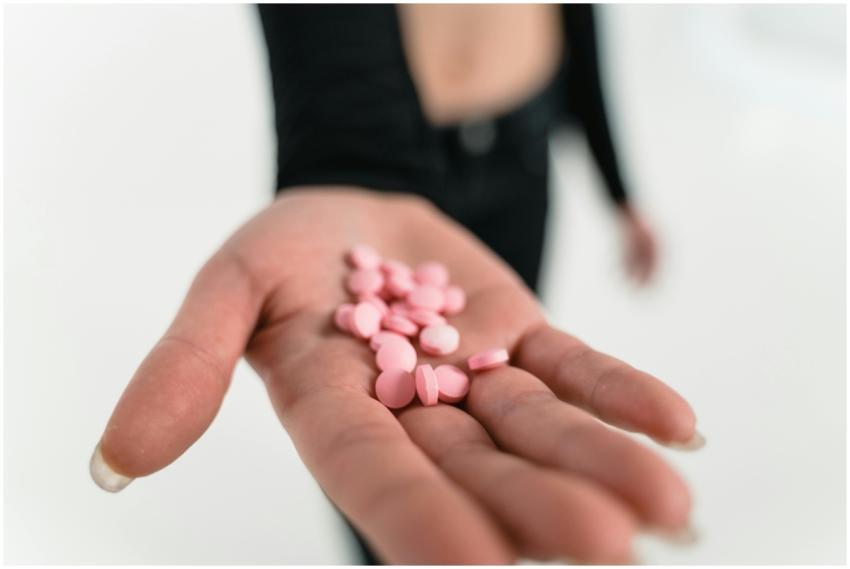 Close-up image of a hand holding pink pills agains