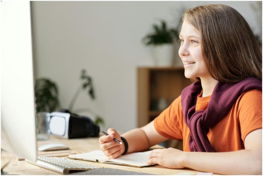 A smiling teenage girl engages in online learning