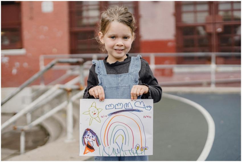 A cheerful child proudly shows her rainbow drawing
