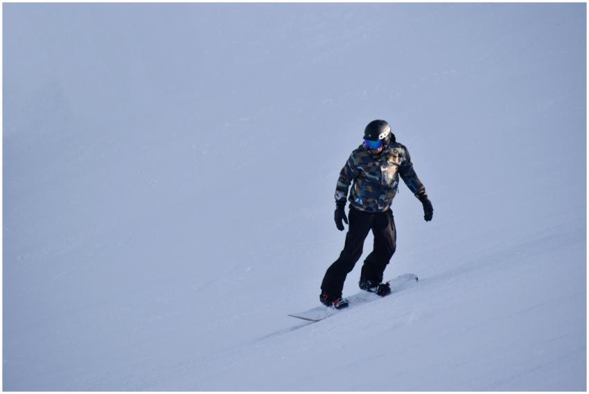 A lone snowboarder descends a snowy slope on a cle