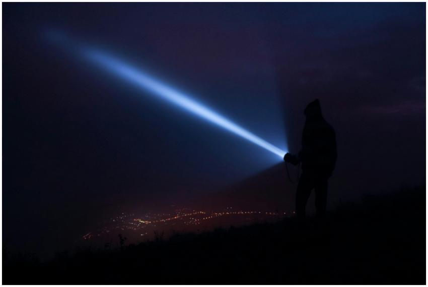 A person holds a flashlight, casting a beam at nig