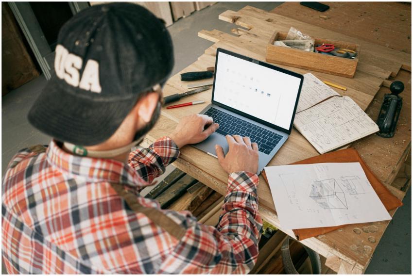 A woodworker in a workshop uses a laptop for furni