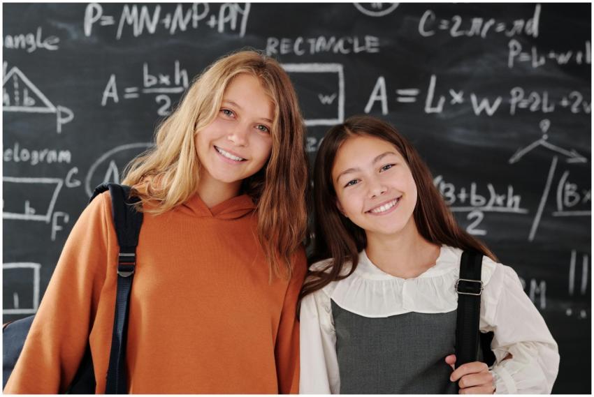 Two cheerful girls stand in a classroom with a mat
