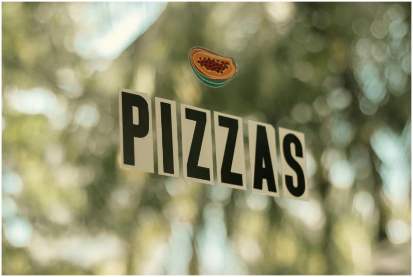 Window sign reading 'PIZZAS' with a blurred outdoo