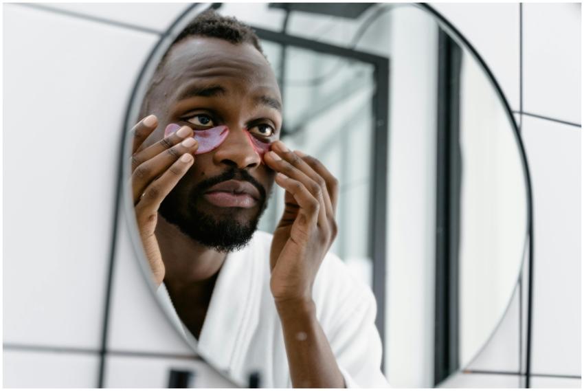 Man in white bathrobe applying eye patches in bath
