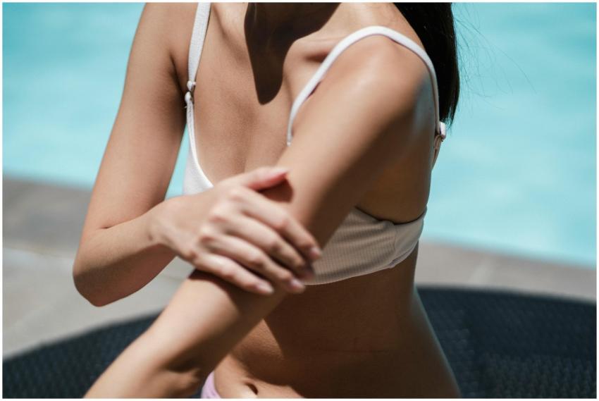 A woman in a swimsuit applies sunscreen by the poo