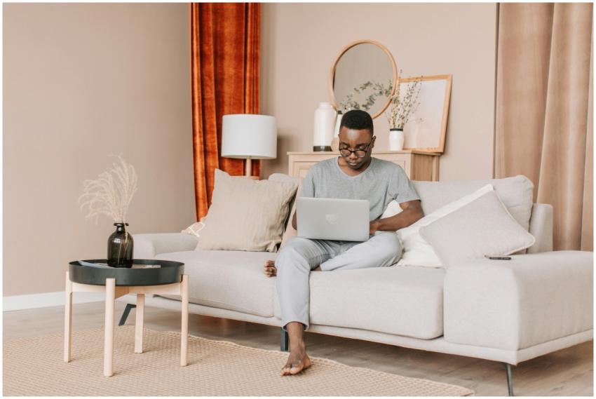 A man sits comfortably on a sofa using his laptop