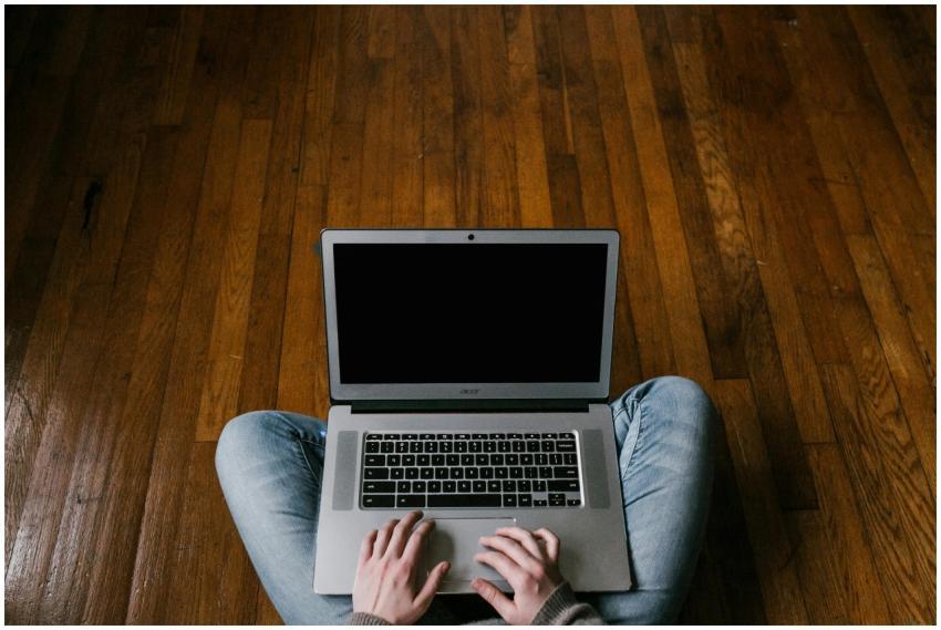 Person sitting cross-legged on hardwood floor usin