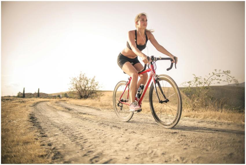 A woman biking on a rural dirt path under the sun,