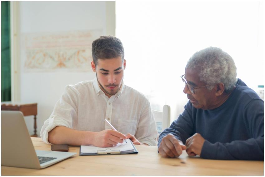 Young man helps elderly man with documents at a de