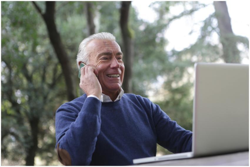 Elderly man joyfully using a laptop and phone outd