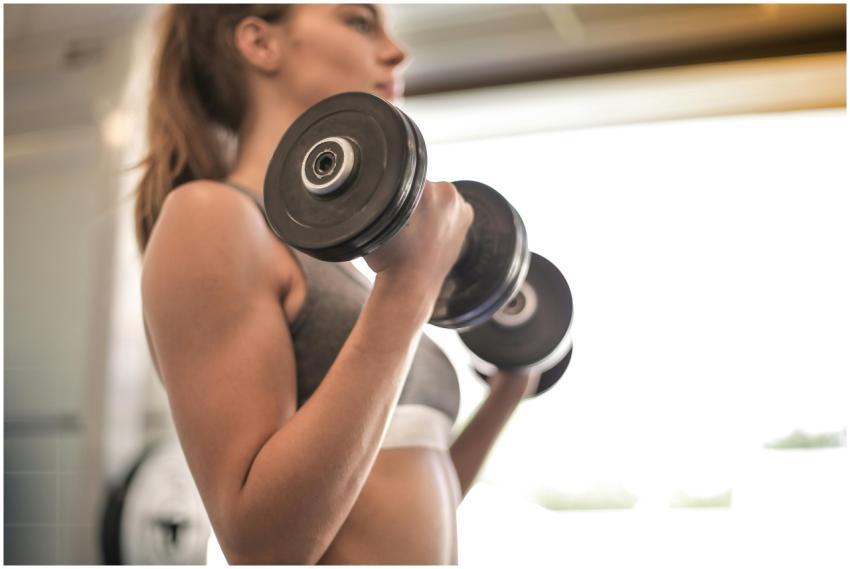 Focused woman lifting dumbbells in a bright gym, e