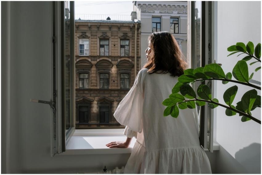 Woman in a white dress looking out an open window