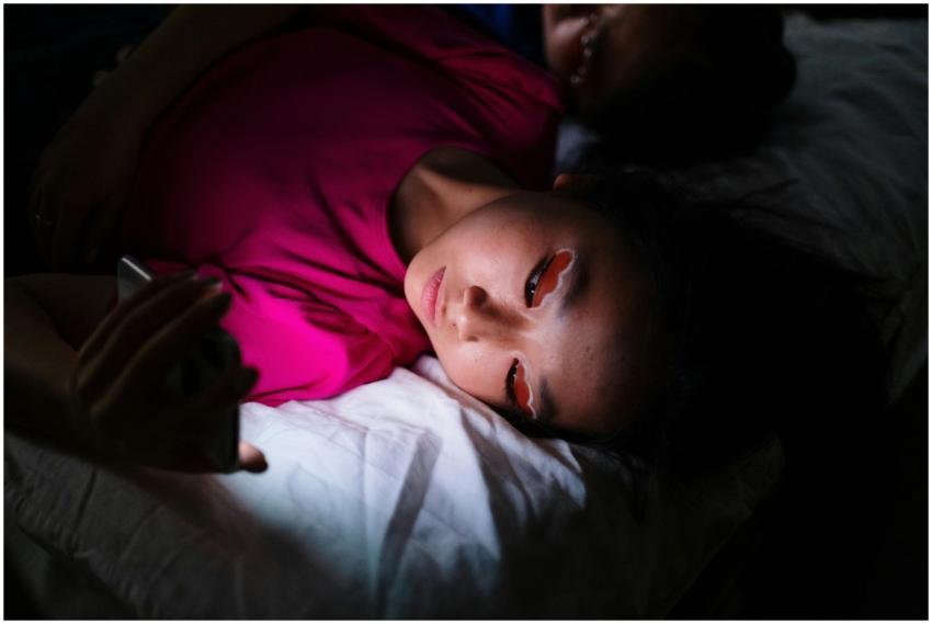 Asian woman lying in bed using smartphone in dark