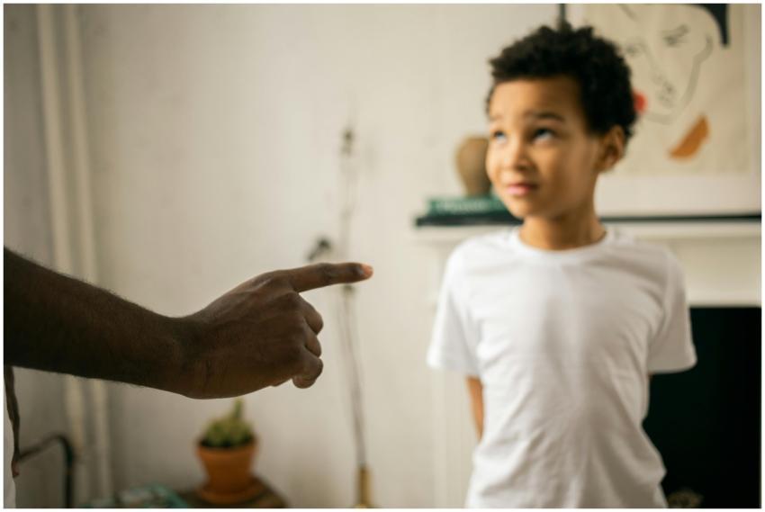 A father points and scolds his son indoors, emphas