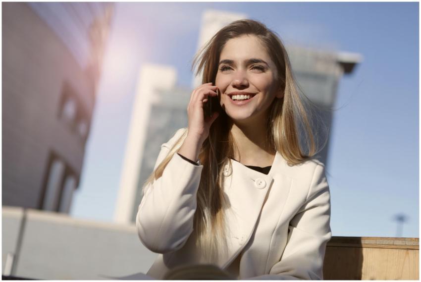 Confident woman in white coat smiling while using
