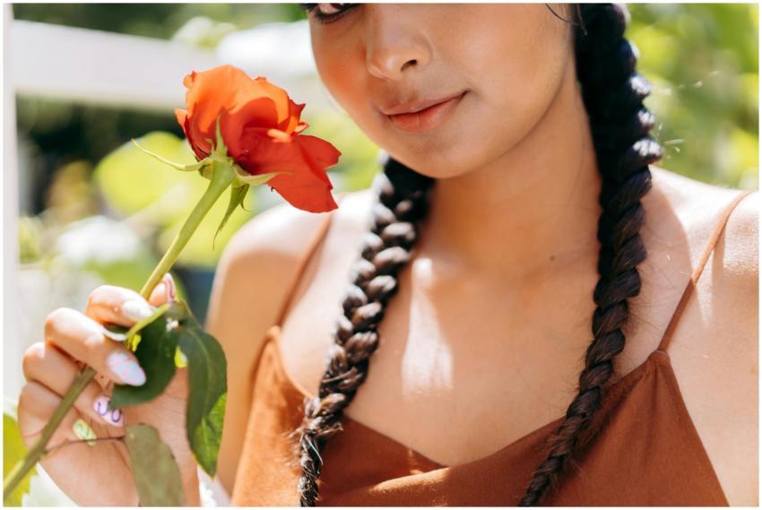 A woman with braided hair holds a vibrant rose, ca