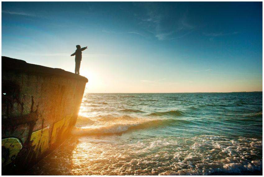A person stands on a cliff overlooking the ocean a