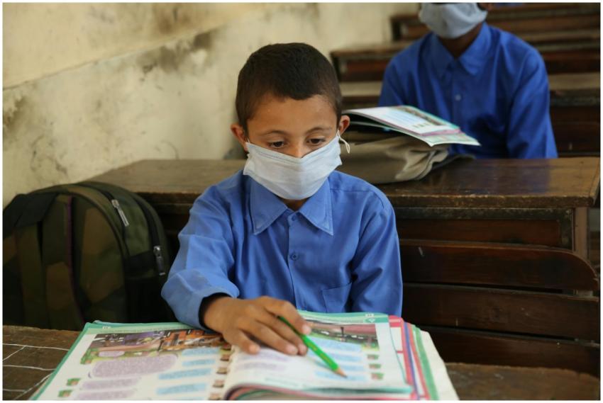 A young boy wearing a mask focuses on his studies
