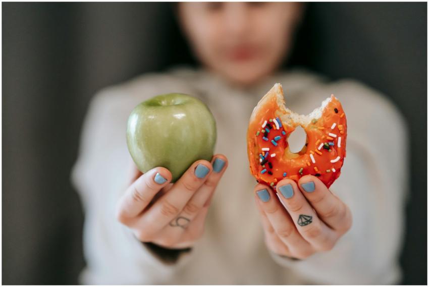 A close-up of a person holding an apple and a donu