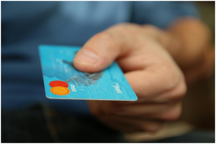 A close-up shot of a hand offering a blue debit ca