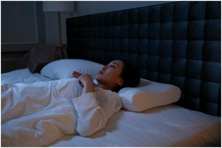 An Asian woman lying awake in bed at night, showin