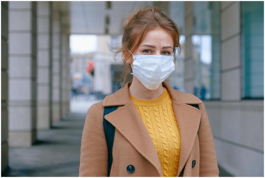 Young woman in a coat and mask stands outdoors, pr