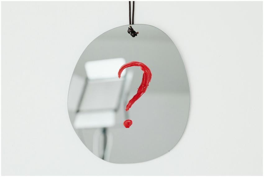 An oval mirror with a red question mark painted on