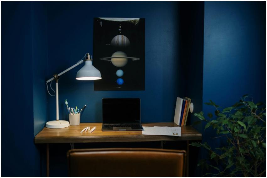 A modern home office with blue walls, desk lamp, a